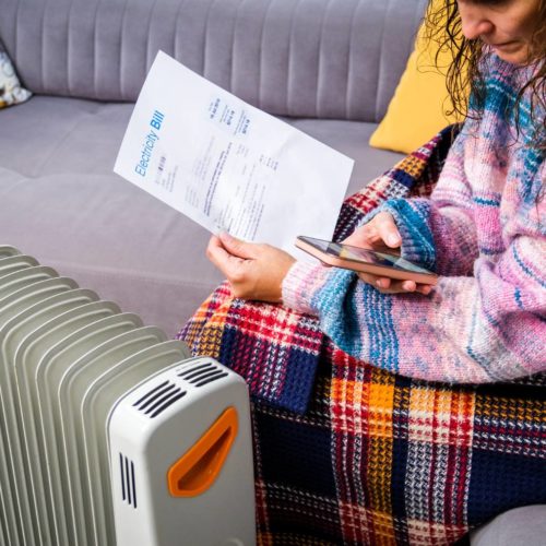 woman sitting by a heater paying energy bill